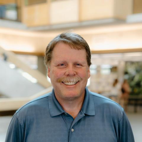 A man with a moustache, dressed in a blue shirt, smiles in the Bata Library atrium.